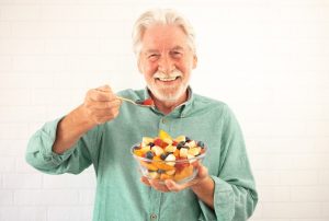 Older man eating a bowl of fruit.