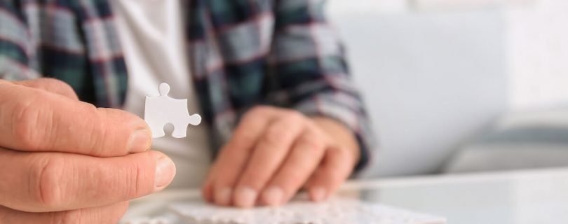 Senior man with Parkinson syndrome doing puzzle at home, closeup